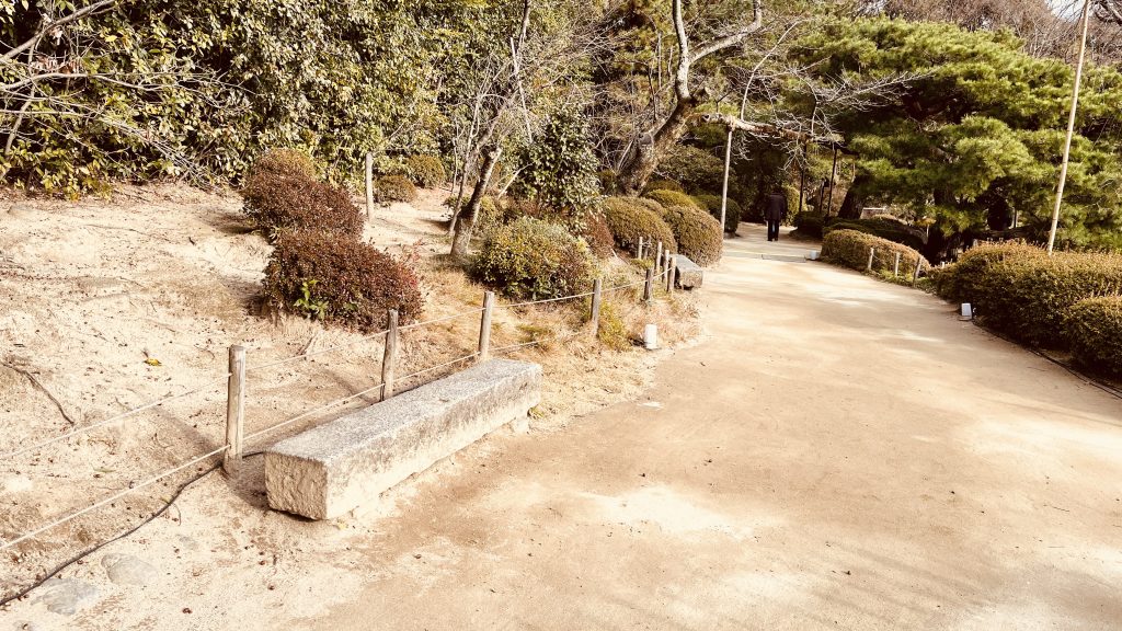 京都・平安神宮神苑の小道に置かれた石のベンチと、静かに続く庭の風景