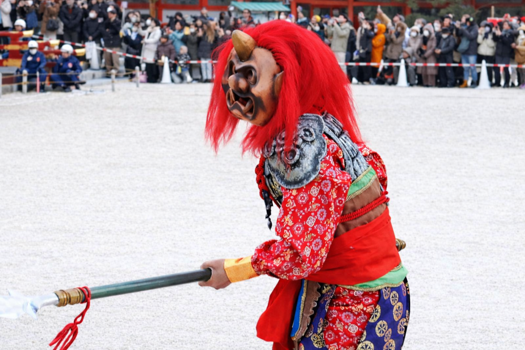 平安神宮の節分行事で、豆を受けながらも引き返してくる鬼。赤い髪と装束を揺らし、再び境内へ向かう場面