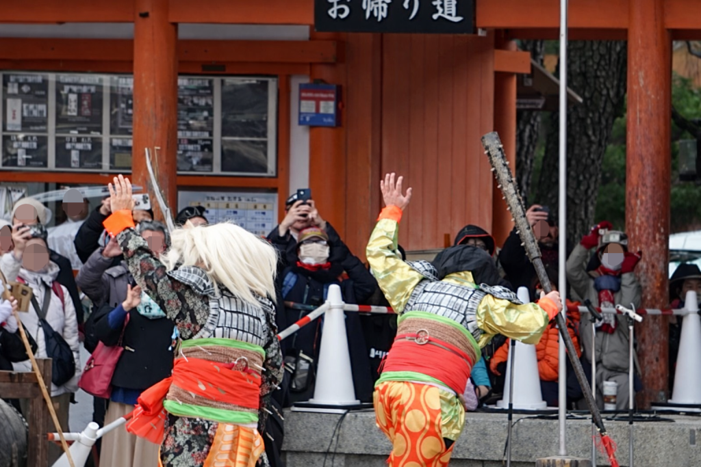 平安神宮の節分行事で、豆を受けながら両手を上げて退散していく鬼たち。参拝者に追われて境内の外へ向かう場面