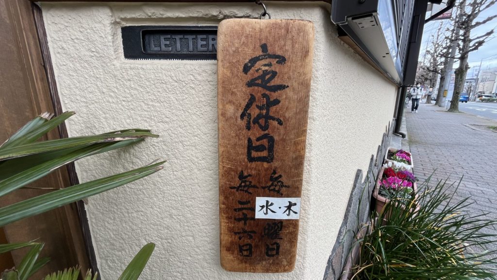 粟餅所澤屋の木製看板に記された水木休みと毎月二十六日の定休日表示