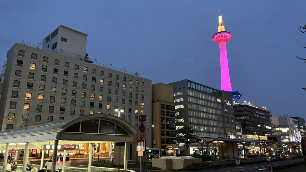 夕暮れ時の京都駅前から望む、ピンク色にライトアップされた京都タワーと周辺のビル群。ピンクは、乳がん啓発。